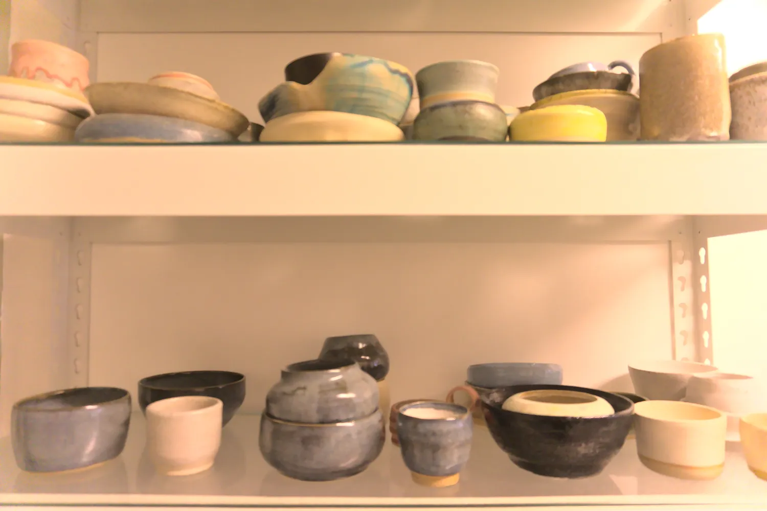 Scaffali con ciotole e tazze di ceramica artigianale dai colori vari