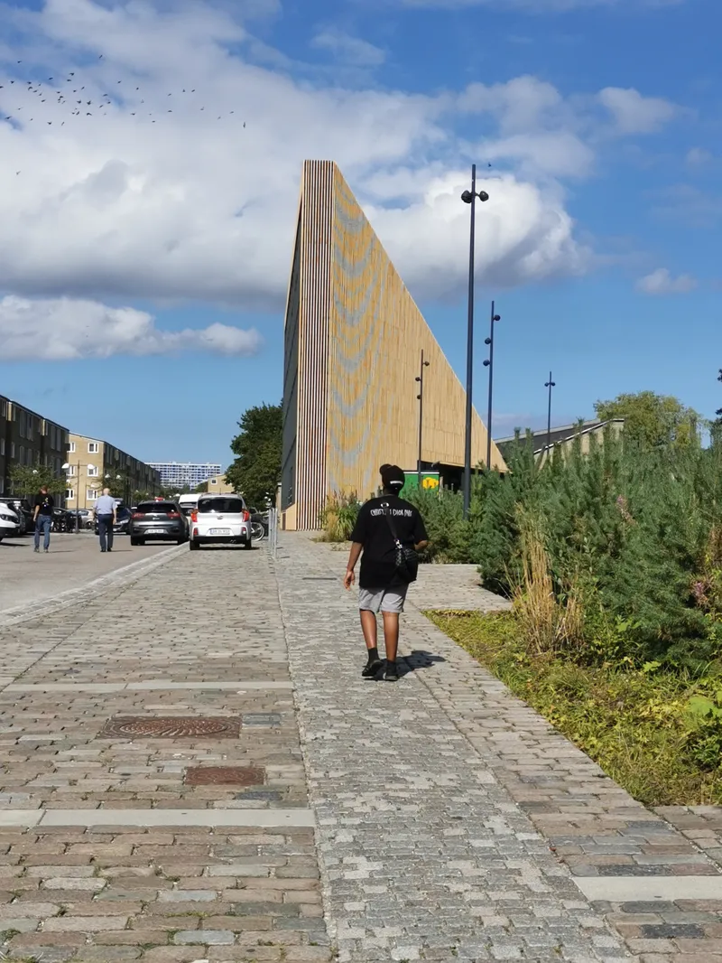 Persona cammina verso la biblioteca Tingbjerg in mattoni gialli e legno