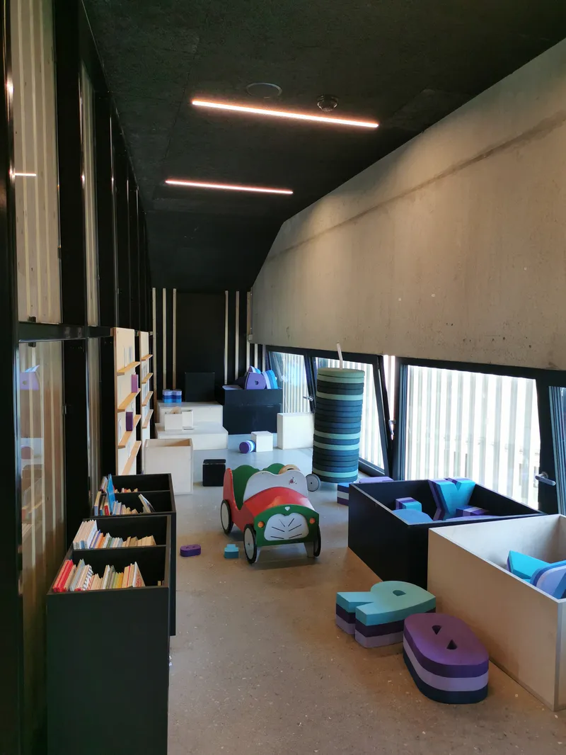Area bambini della biblioteca Tingbjerg con automobilina e cuscini colorati