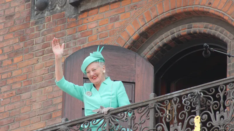 Donna anziana in abito verde saluta dal balcone di un edificio in mattoni