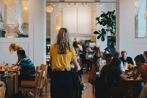Persone sedute ai tavoli in legno di un luminoso caffè-ristorante