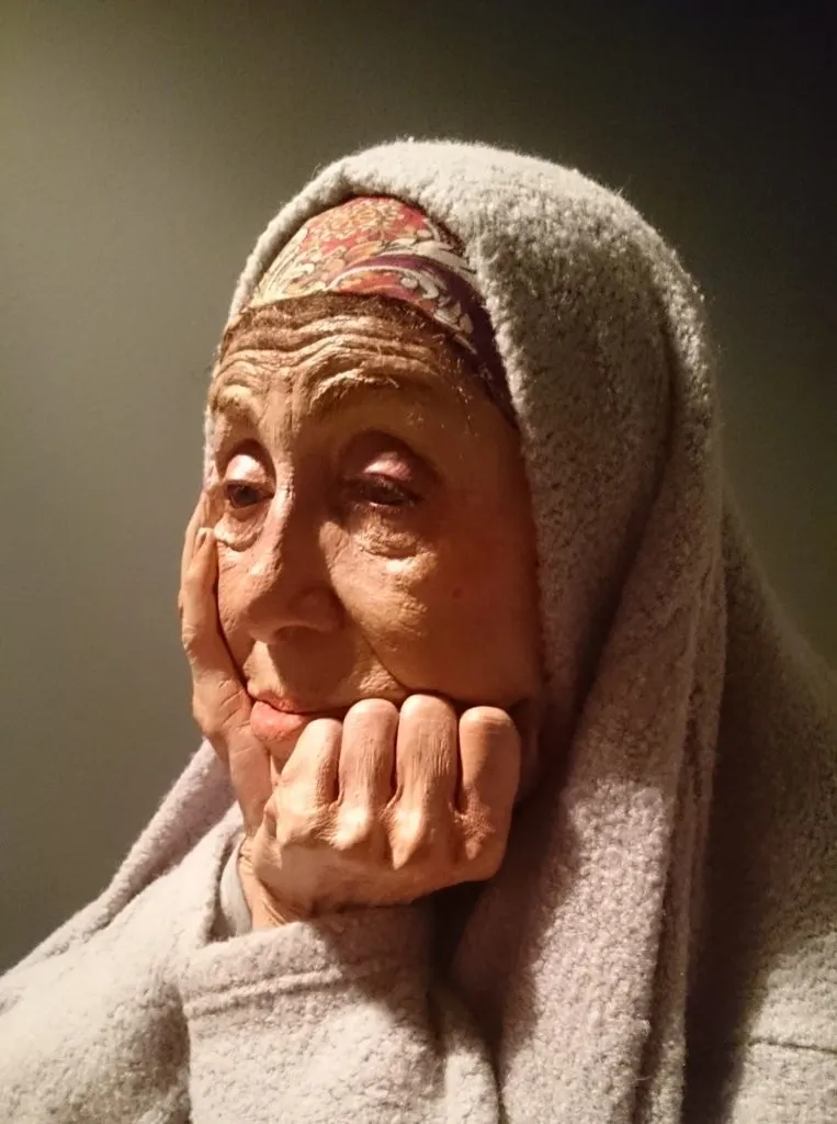Scultura iperrealistica del volto di una donna anziana col capo coperto
