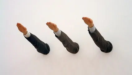 Ave Maria di Maurizio Cattelan: tre braccia in maniche da abito sporgono dal muro bianco salutando