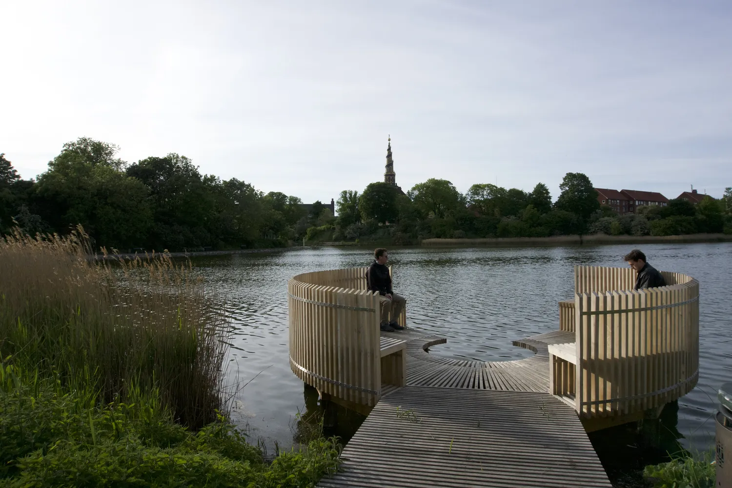 Pontile circolare in legno su un lago con guglia di chiesa lontana