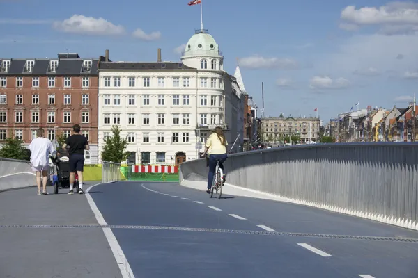Ciclista e pedoni su un ponte azzurro verso palazzi storici