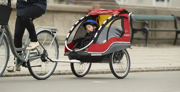 Bambino con casco dorme nel rimorchio rosso Winther trainato da bicicletta