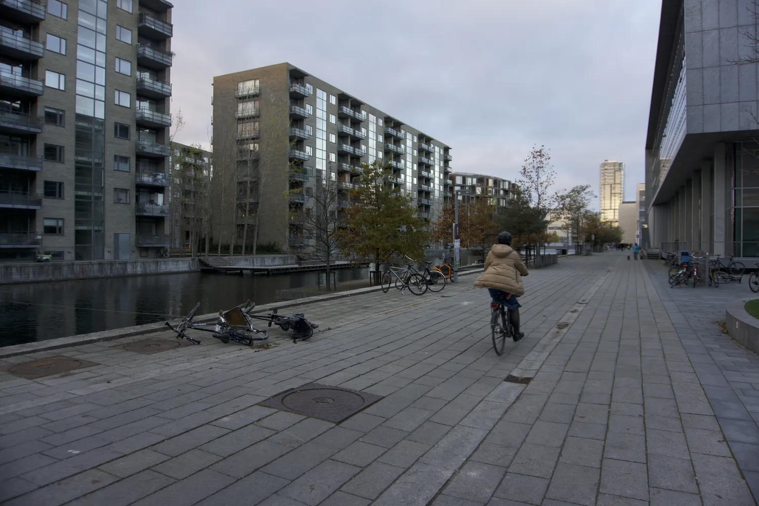 Ciclista lungo un canale tra moderni palazzi in mattoni del quartiere Ørestad