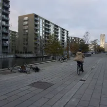 Ciclista lungo un canale tra moderni palazzi in mattoni del quartiere Ørestad