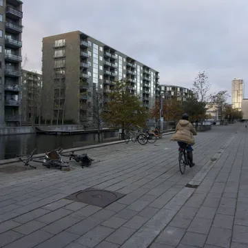 Ciclista lungo un canale tra moderni palazzi in mattoni del quartiere Ørestad