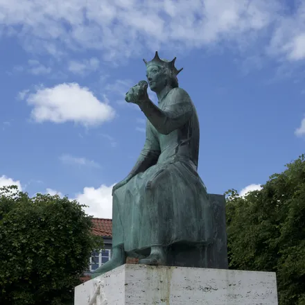 Statua bronzea di re con corona seduto, contro un cielo azzurro