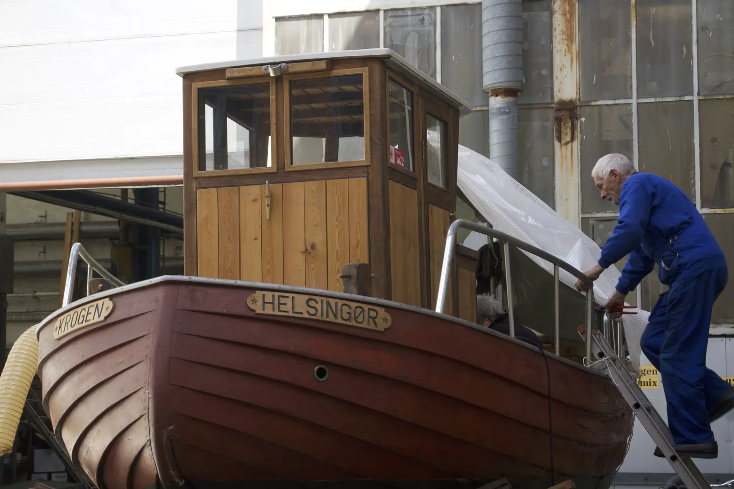 Uomo copre con un telo una barca di legno chiamata Helsingor