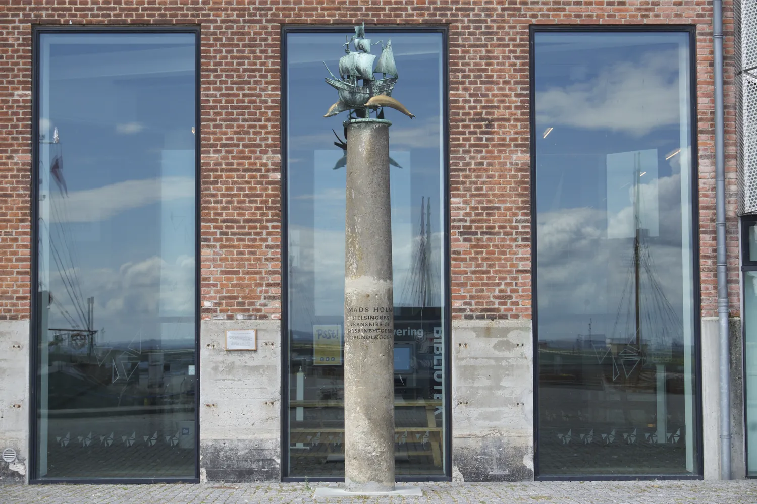 Colonna con scultura di nave in bronzo davanti a vetrate di mattoni rossi a Helsingør