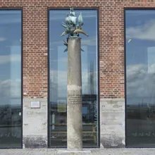 Colonna con scultura di nave in bronzo davanti a vetrate di mattoni rossi a Helsingør