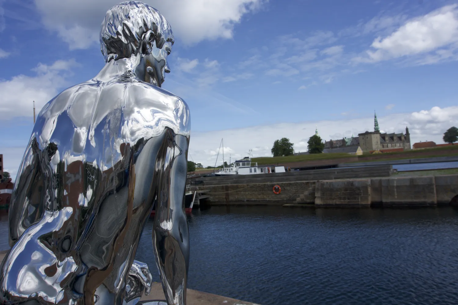 Statua umana in metallo lucido sul lungomare di Helsingør con il Castello di Kronborg in lontananza