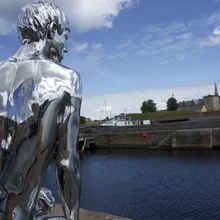 Statua umana in metallo lucido sul lungomare di Helsingør con il Castello di Kronborg in lontananza