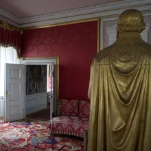 Statua dorata vista di spalle in una sala con pareti rosse damascate