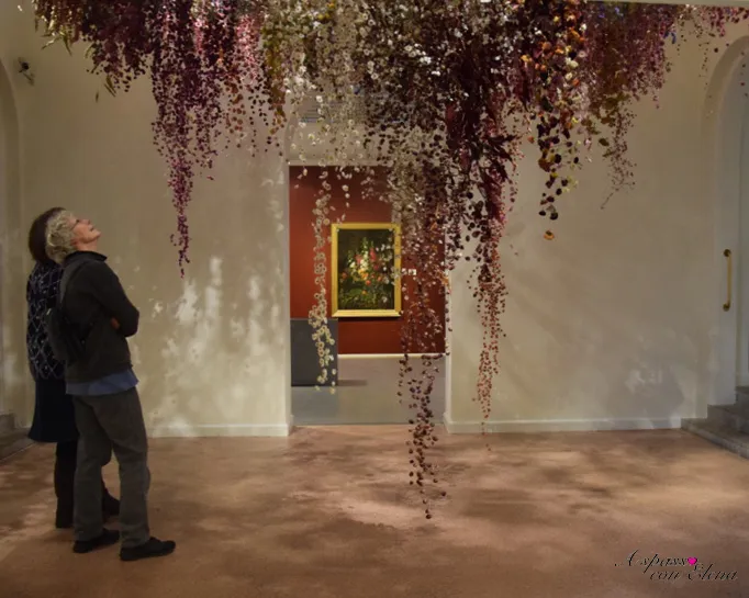 Visitatrice osserva Nature Morte di Rebecca Louise Law, installazione di fiori sospesi