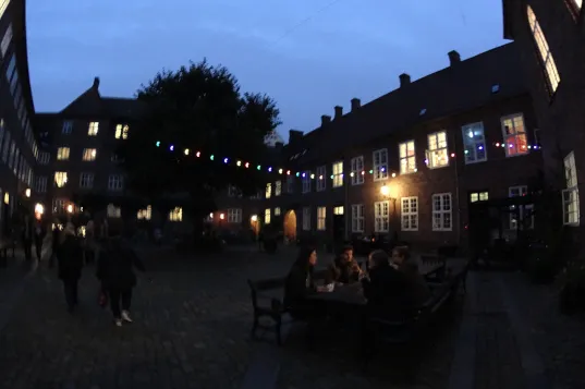 Cortile serale con luci colorate e persone a un tavolo durante la Notte della Cultura