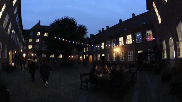 Cortile serale con luci colorate e persone a un tavolo durante la Notte della Cultura