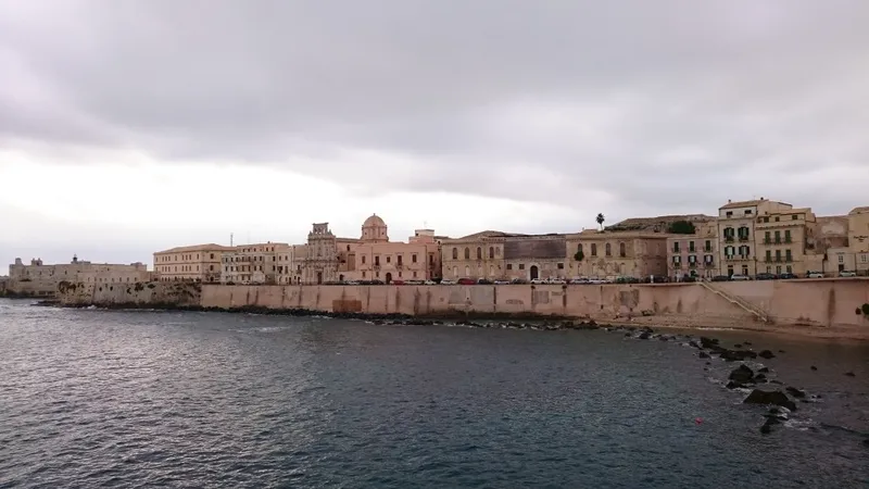 Lungomare di Ortigia a Siracusa visto dal mare sotto cielo grigio
