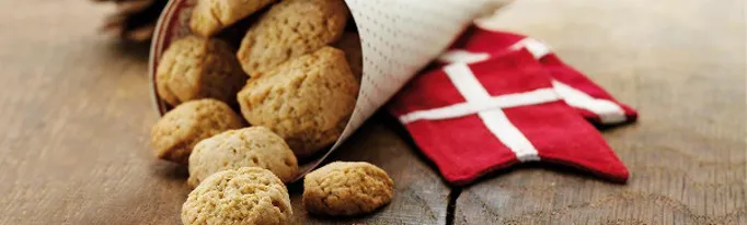 Biscotti danesi pebernød usciti da un cono di carta accanto a una bandiera danese