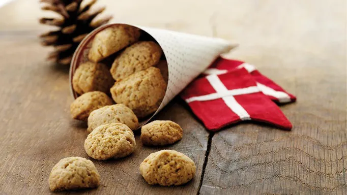 Biscotti danesi pebernød usciti da un cono di carta accanto a una bandiera danese