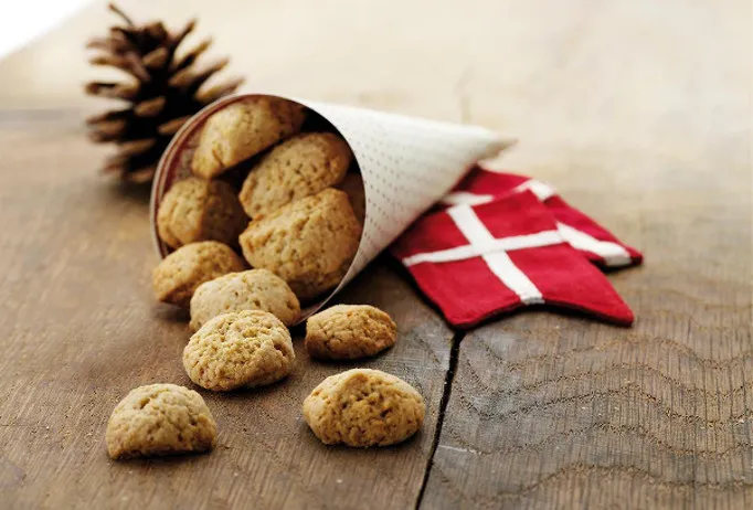 Biscotti danesi pebernød usciti da un cono di carta accanto a una bandiera danese