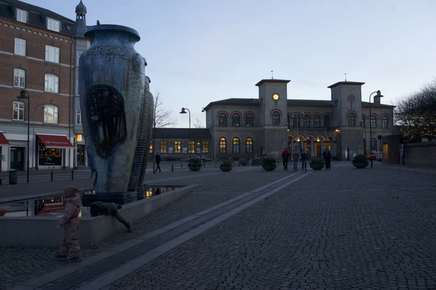 Scultura a forma di vaso in una piazza con la stazione storica sullo sfondo