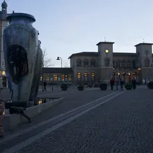 Scultura a forma di vaso in una piazza con la stazione storica sullo sfondo