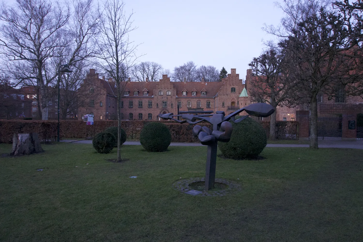 Scultura moderna in un giardino davanti a un edificio storico in mattoni