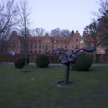 Scultura moderna in un giardino davanti a un edificio storico in mattoni
