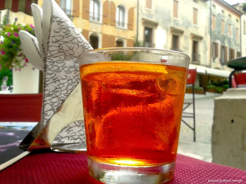 Glass of orange Venetian spritz on a table in a town square