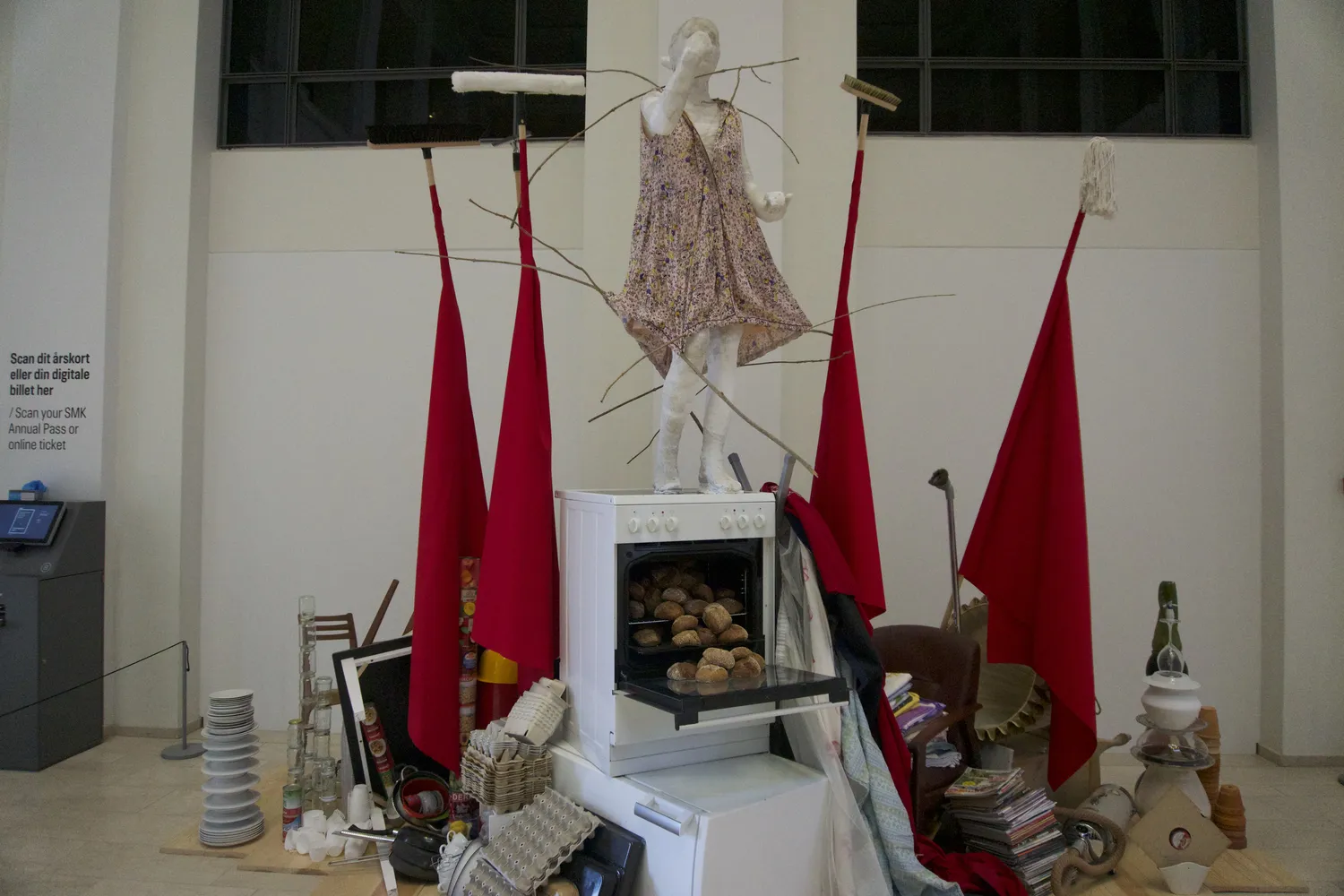 Installazione artistica con figura in abito, bandiere rosse e forno