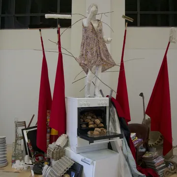 Installazione artistica con figura in abito, bandiere rosse e forno