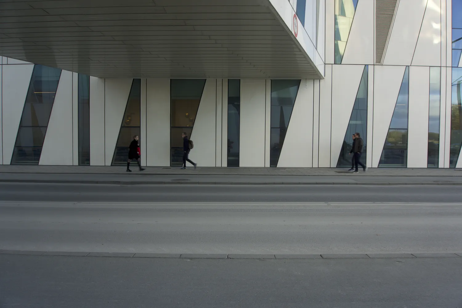 Persone camminano davanti a un edificio bianco con vetrate inclinate a Ørestad