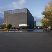 Edificio cubico scuro con facciata traforata accanto a un bacino d'acqua a Ørestad