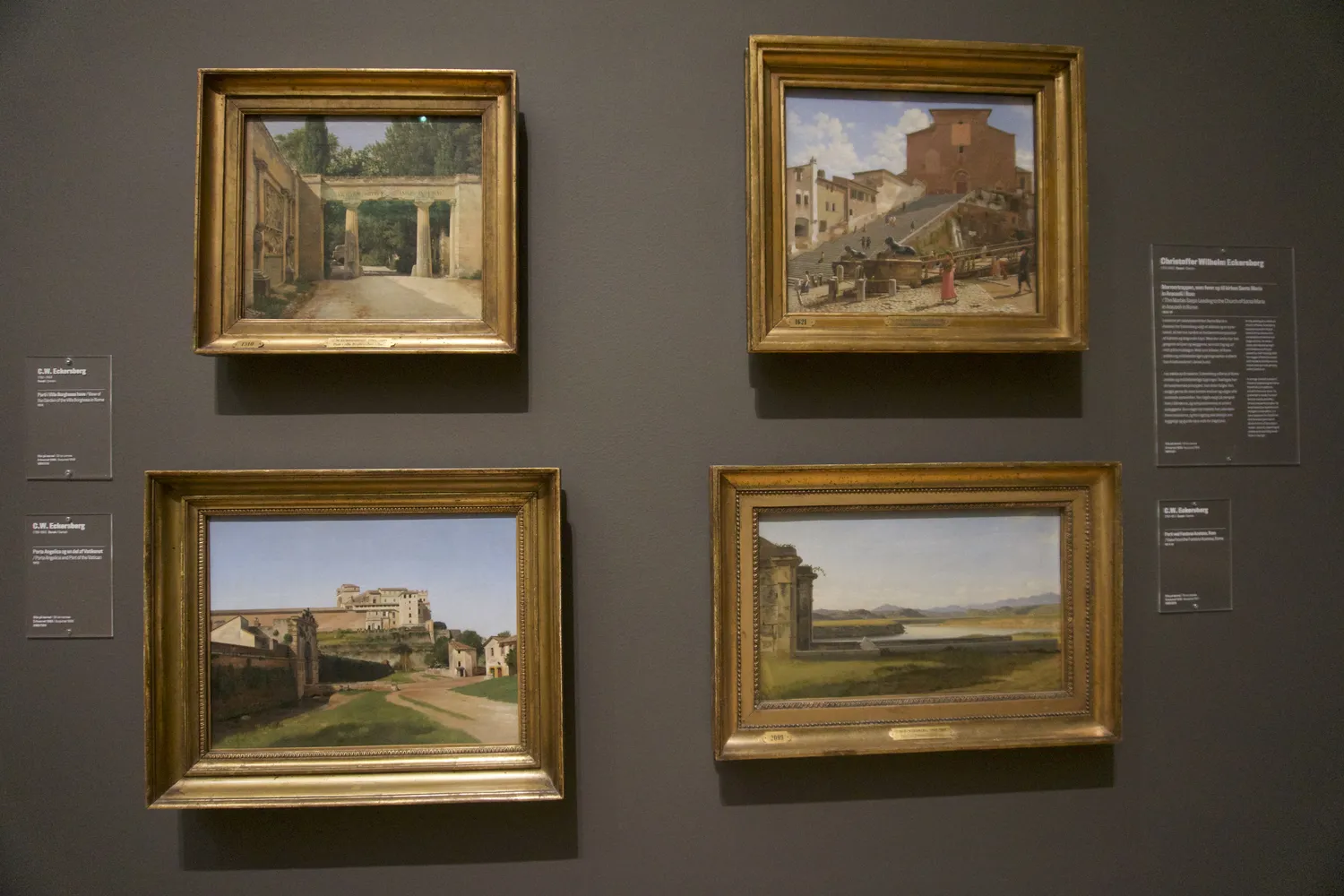 Quattro dipinti incorniciati di paesaggi italiani su parete grigia di museo