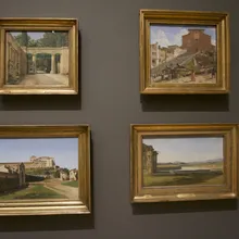 Quattro dipinti incorniciati di paesaggi italiani su parete grigia di museo
