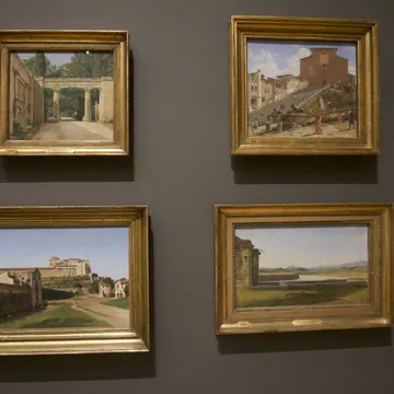 Quattro dipinti incorniciati di paesaggi italiani su parete grigia di museo