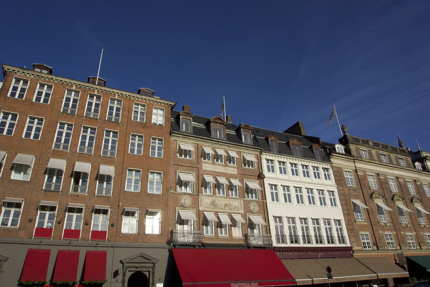Facciate storiche di palazzi in mattoni con tende rosse a Copenaghen sotto un cielo azzurro