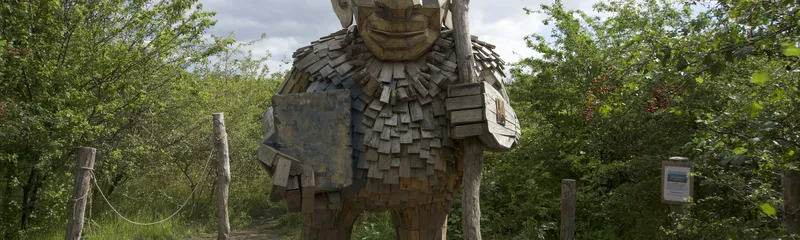Troll gigante di legno con bastone su un sentiero tra gli alberi