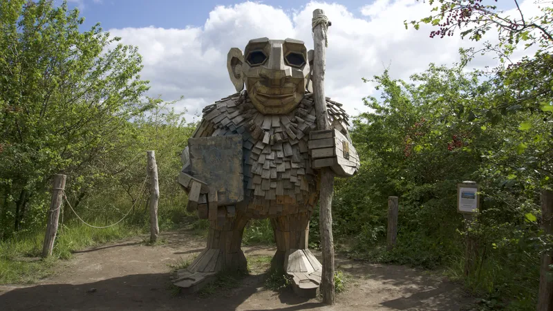 Troll gigante di legno con bastone su un sentiero tra gli alberi