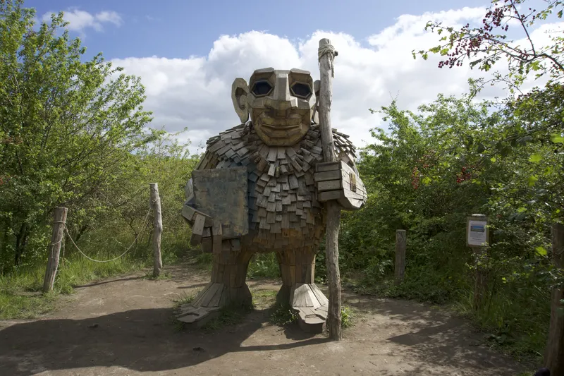 Troll gigante di legno con bastone su un sentiero tra gli alberi