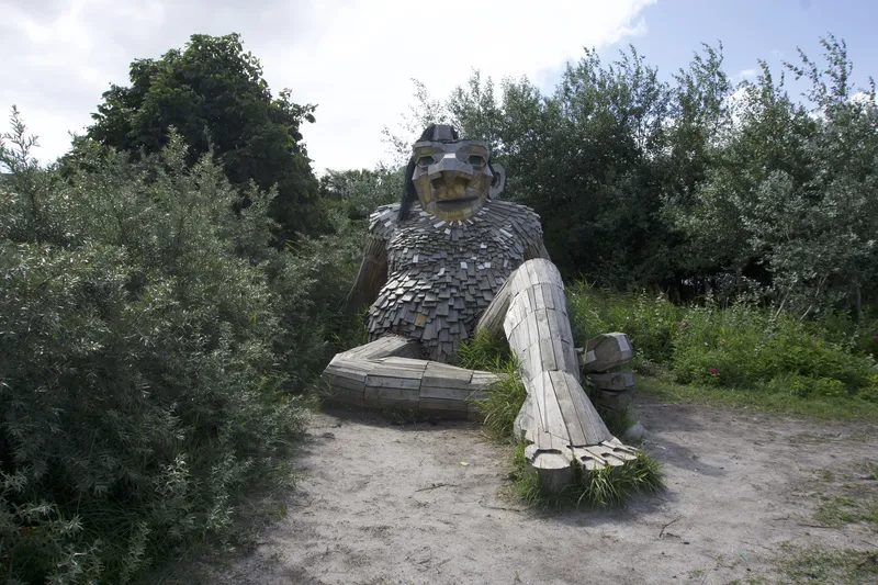 Troll gigante di legno seduto tra cespugli verdi