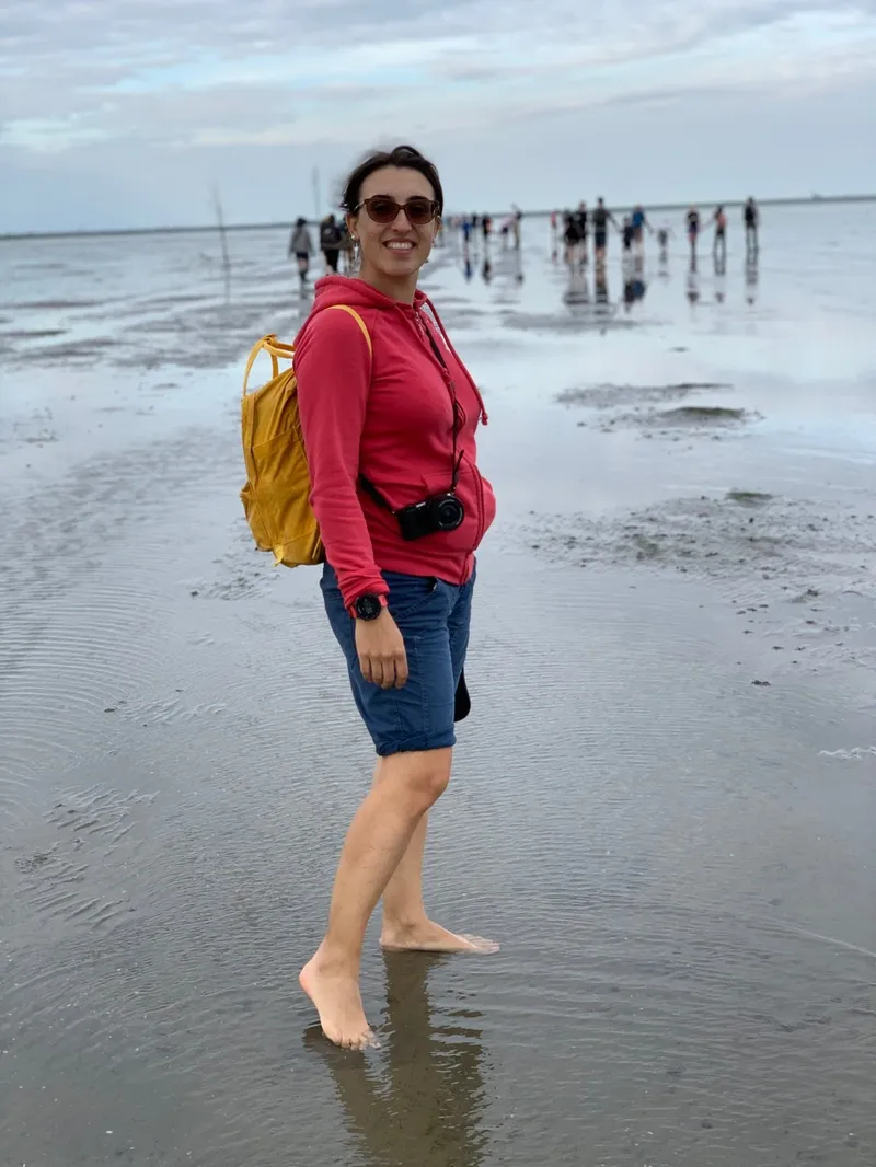 Donna con felpa rossa e zaino giallo sul fondale del Vadehavet in bassa marea