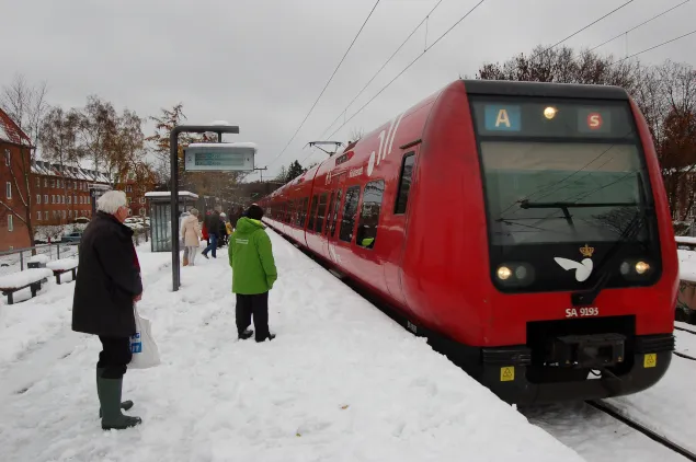 Treno rosso danese in stazione innevata con persone in attesa