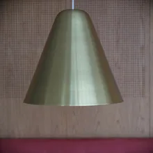 Lampada a sospensione conica in ottone davanti a parete in legno